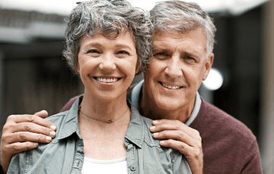 Older couple smiling after replacing missing teeth