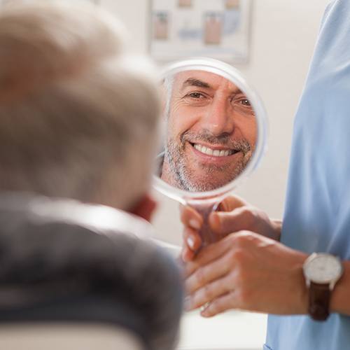 Man looking at smile in mirror after full mouth reconstruction