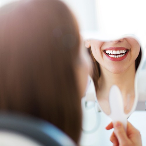 Woman looking at smile after metal free dental restoration placement