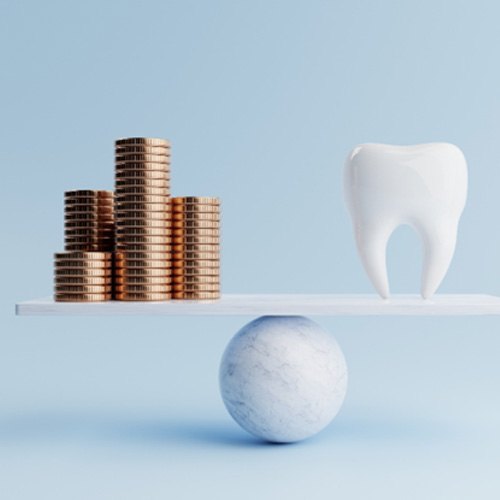 A model tooth and golden coins on a balancing scale
