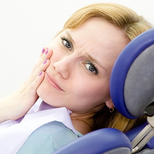 A woman lying back in the dentist’s chair holding her cheek because of a dental emergency in Midlothian