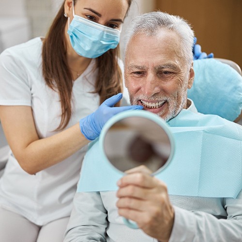 An older man looking at his new smile in the mirror while a dental hygienist points to his dental implant