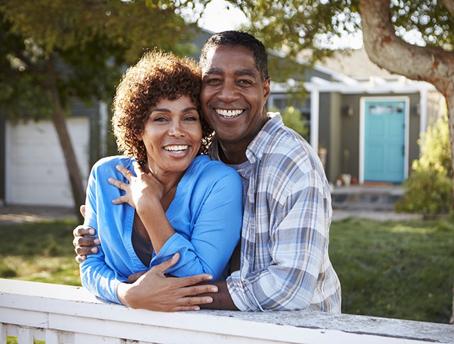 couple with dental implants in Midlothian smiling on their front porch 