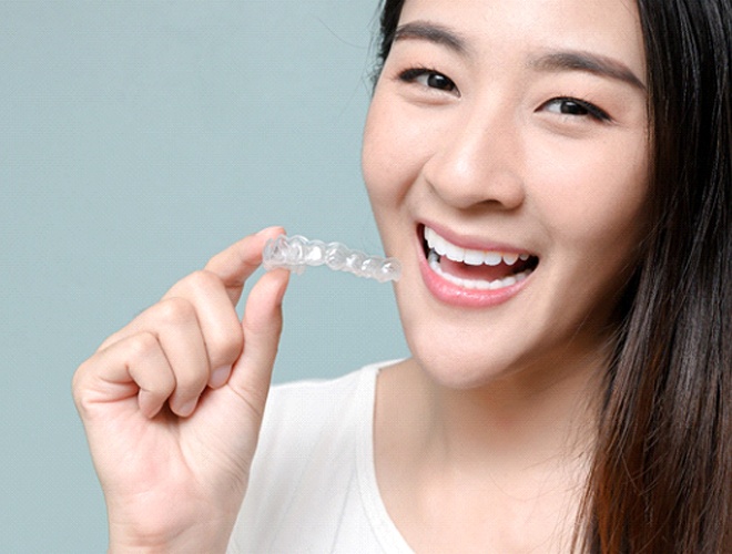 person smiling and holding Invisalign trays