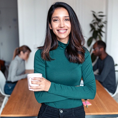 person smiling and holding a cup of coffee while standing in their break room at work