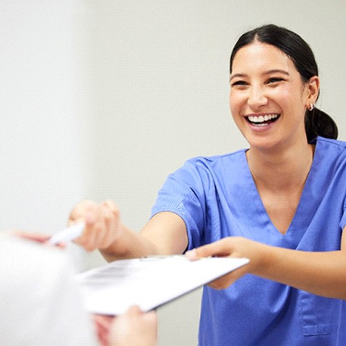 Dental assistant smiling while handing patient form