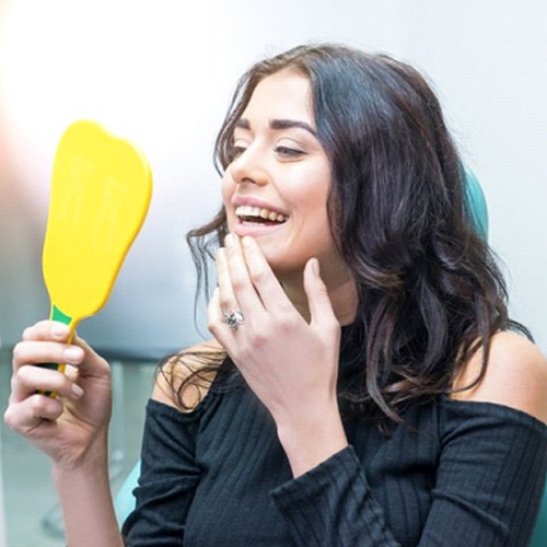 patient admiring her smile in a mirror after getting her teeth whitened
