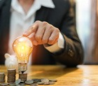 Man tapping a lightbulb that’s sitting on a pile of coins