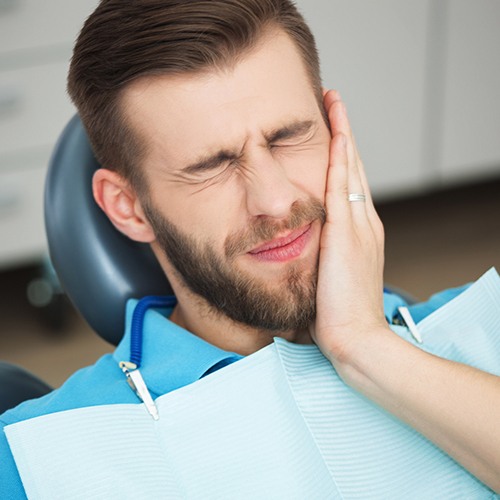 Young man in need of wisdom tooth extraction holding jaw